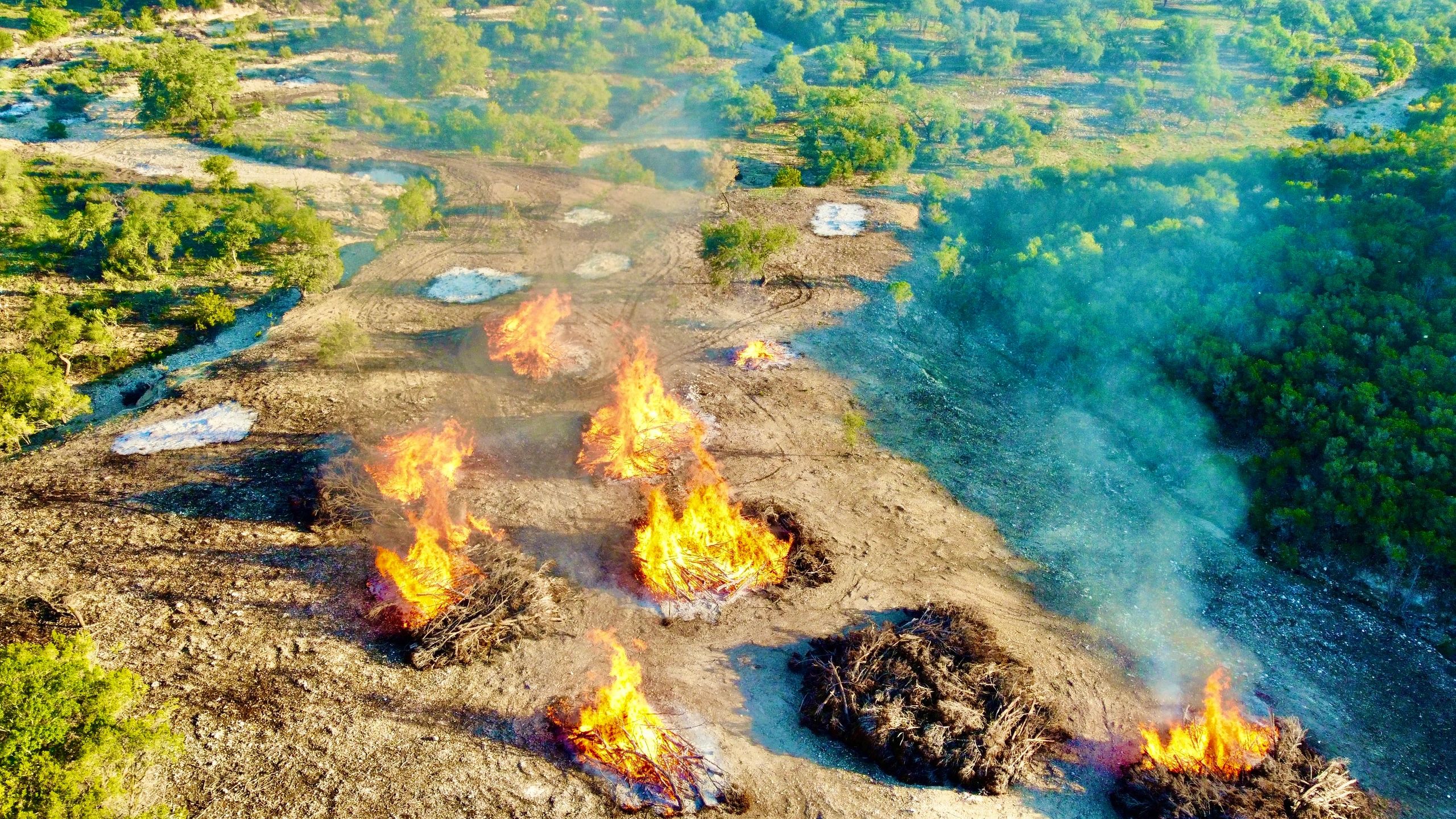 Large piles of cedar being burned in a clearing and reclamation process for large ranch owner