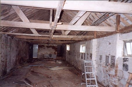 Empty, rundown interior of a building with exposed beams and debris.