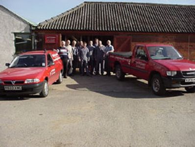 Group of people standing between two red vehicles outside a building.