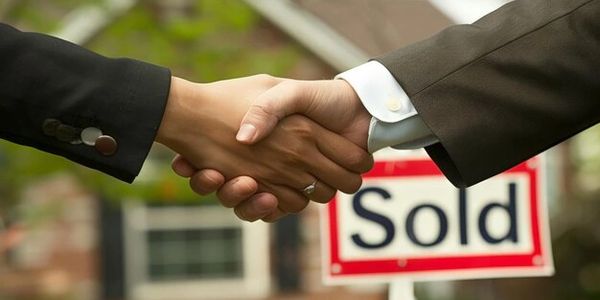 Two people shaking hands in front of a sold sign.