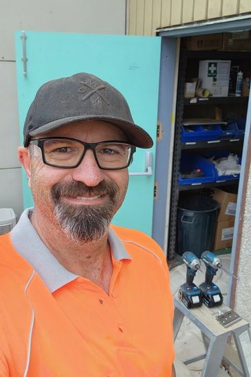A portrait of Dave standing smiling outside wearing glasses, a cap and hivis polo top. 