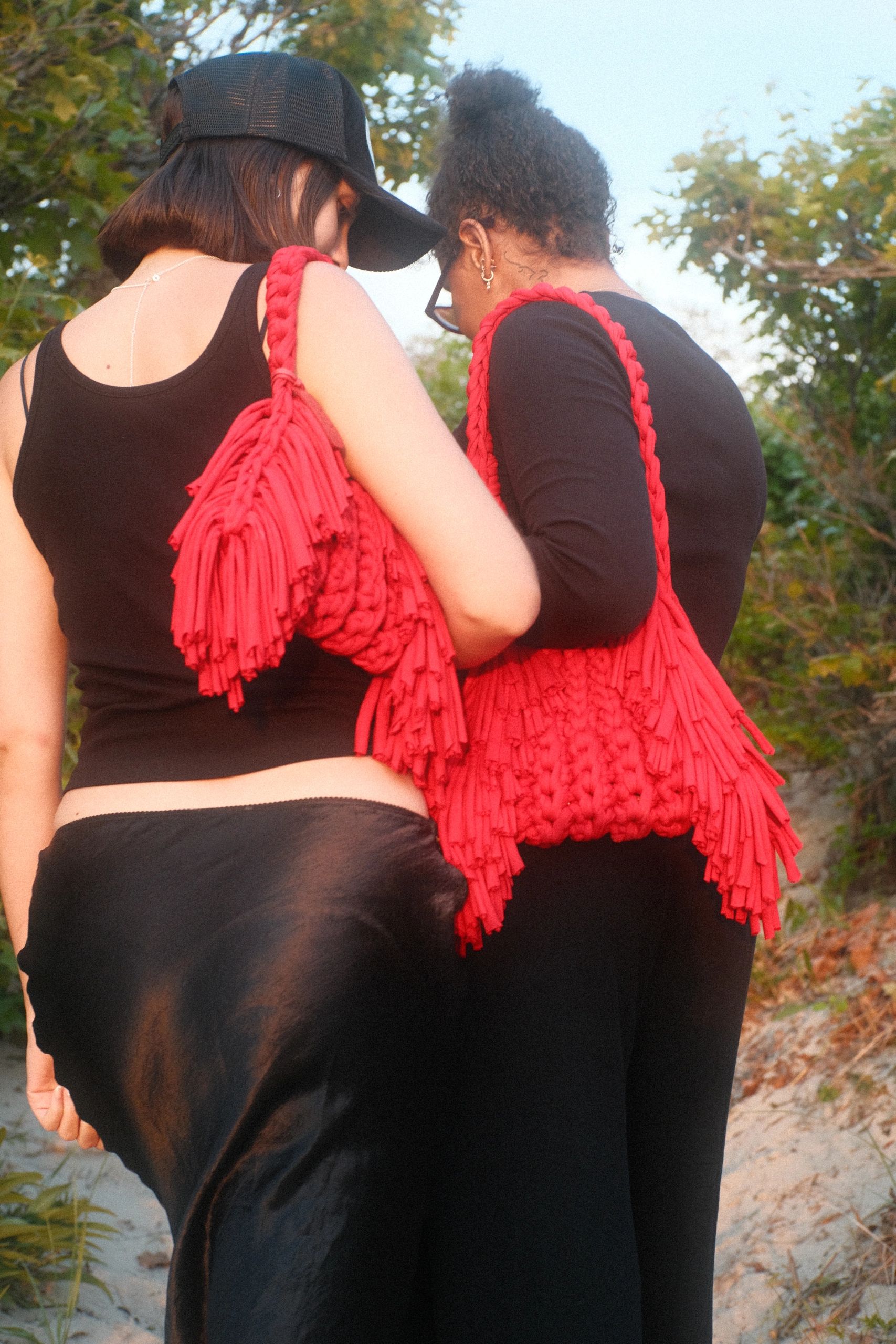 Two women wearing black outfits and carrying red textured bags outdoors.