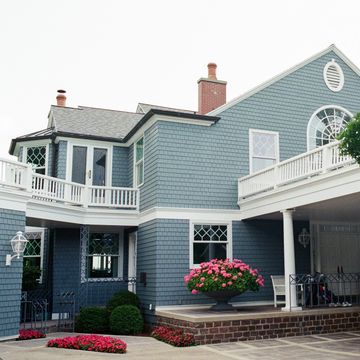 Blue two-story house with white railings and pink flowers.