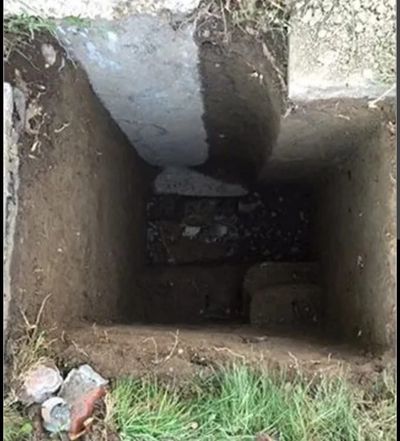 Deep rectangular hole dug in the ground.