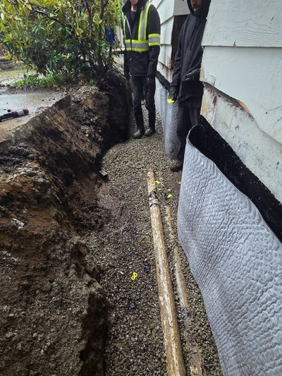 Utility excavation trench beside a Nanaimo home with exposed service lines and gravel base.
