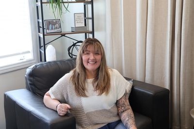 A woman with a tattooed arm sits smiling on a black leather couch.