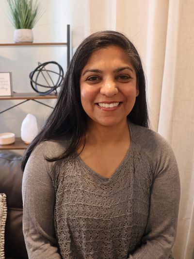 Smiling woman in a cozy room with a decorative shelf behind her.