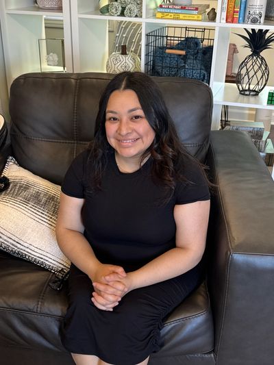 Woman smiling and sitting on a dark leather couch indoors.