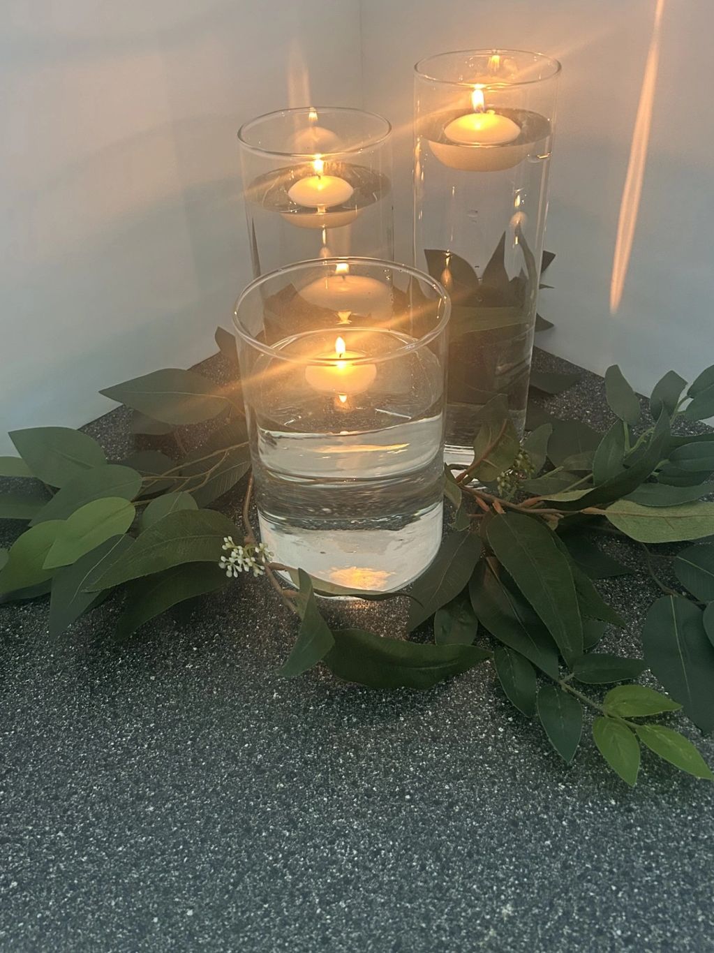 Floating candles in glass vases surrounded by greenery.