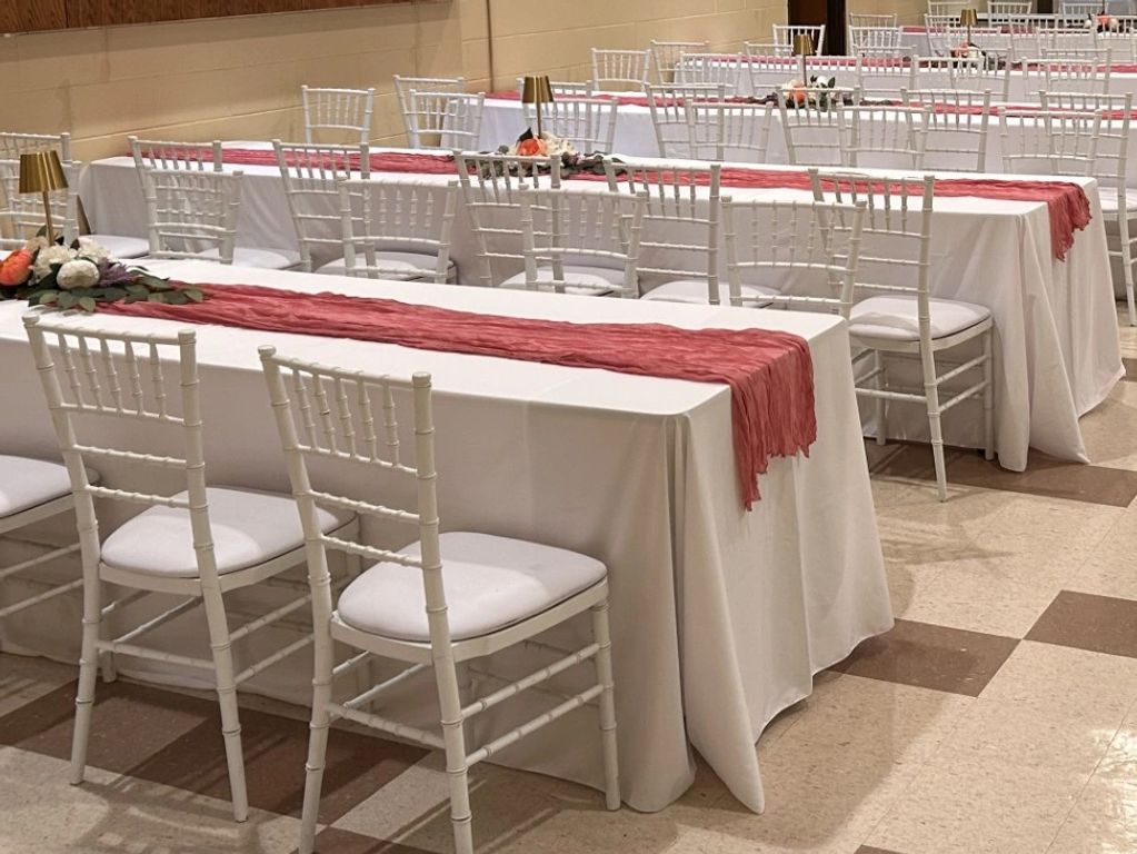 Decorated banquet tables with white chairs and pink runners.