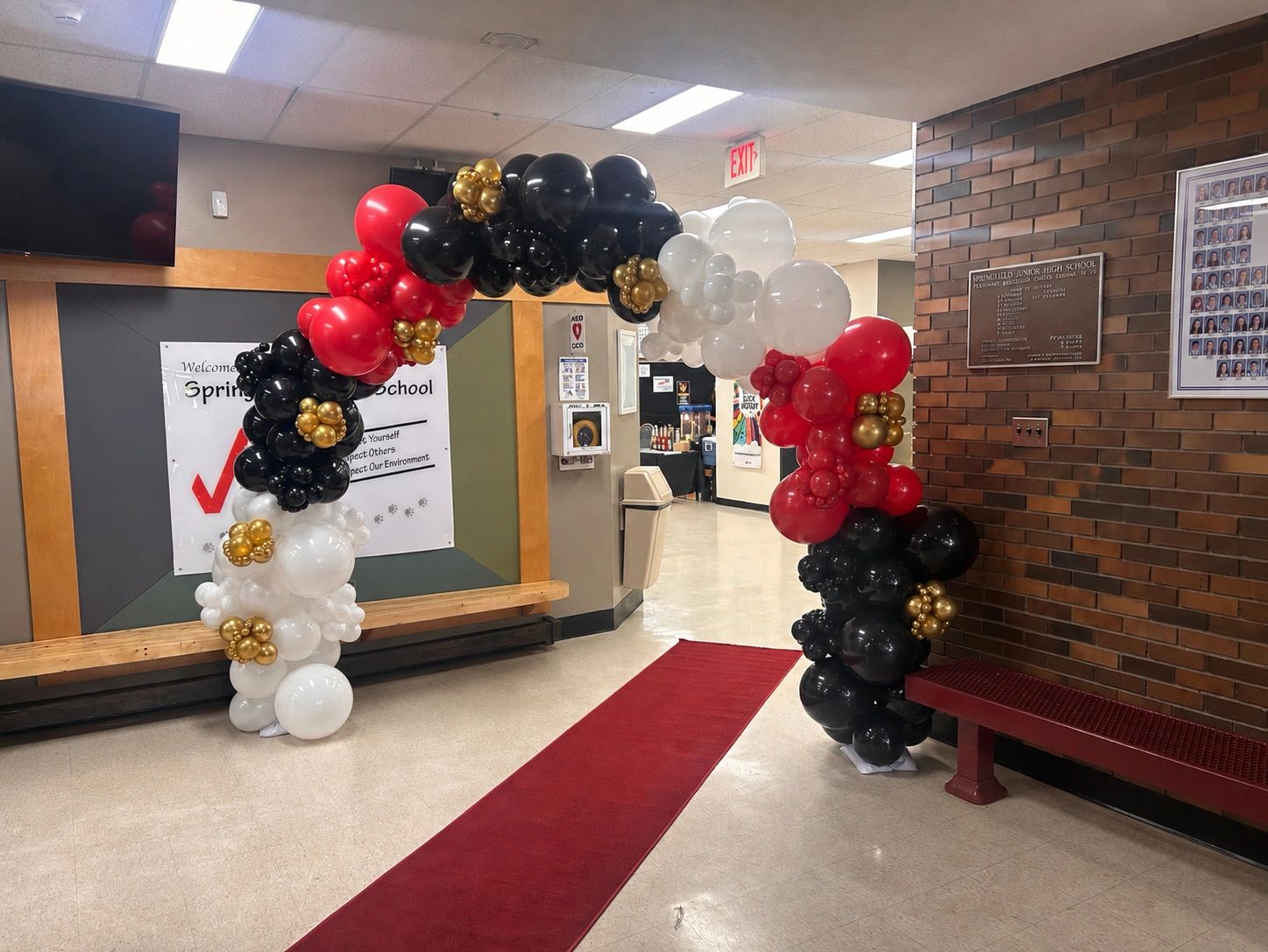 Balloon arch with red carpet in a school hallway.