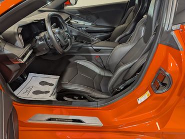 Interior of a Corvette Stingray with black leather seats and orange door frame.