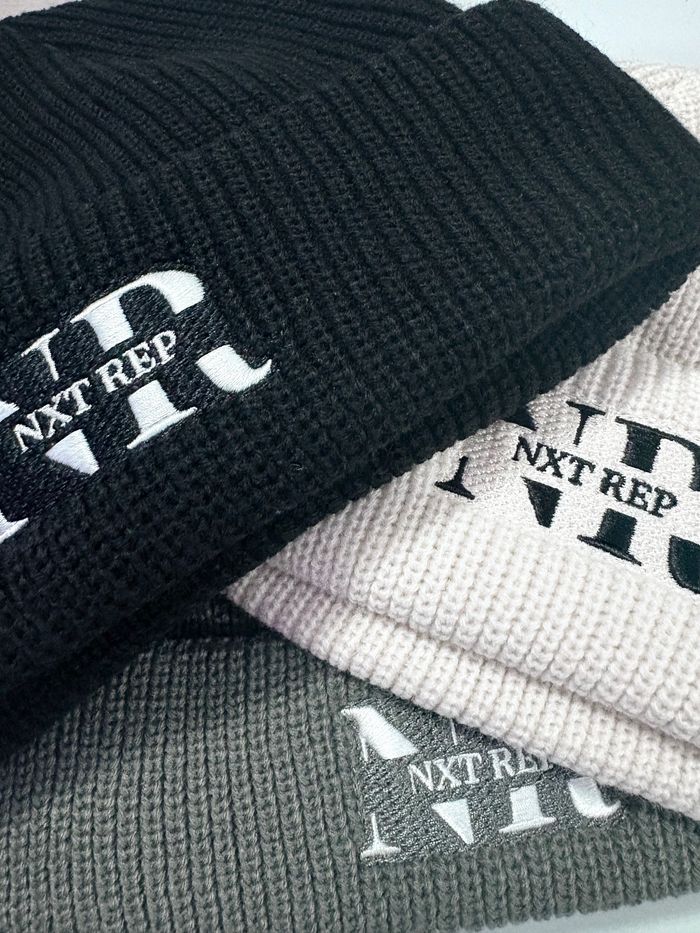 Three knitted beanies in black, white, and gray with 'NXT REP' embroidered on them.