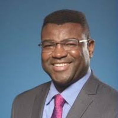 Man in glasses smiling in suit and tie against blue background.