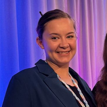 Smiling woman in blue blazer with colorful lanyard.