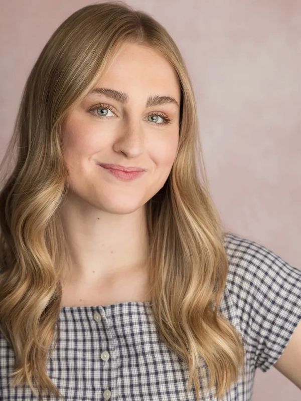 Young woman with long blonde hair smiling against a soft pink background.