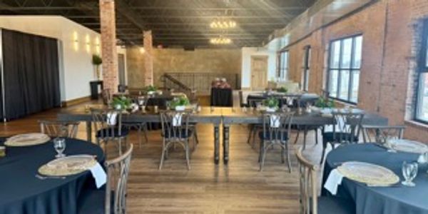 Elegant event room set with tables, black linens, and rustic decor.