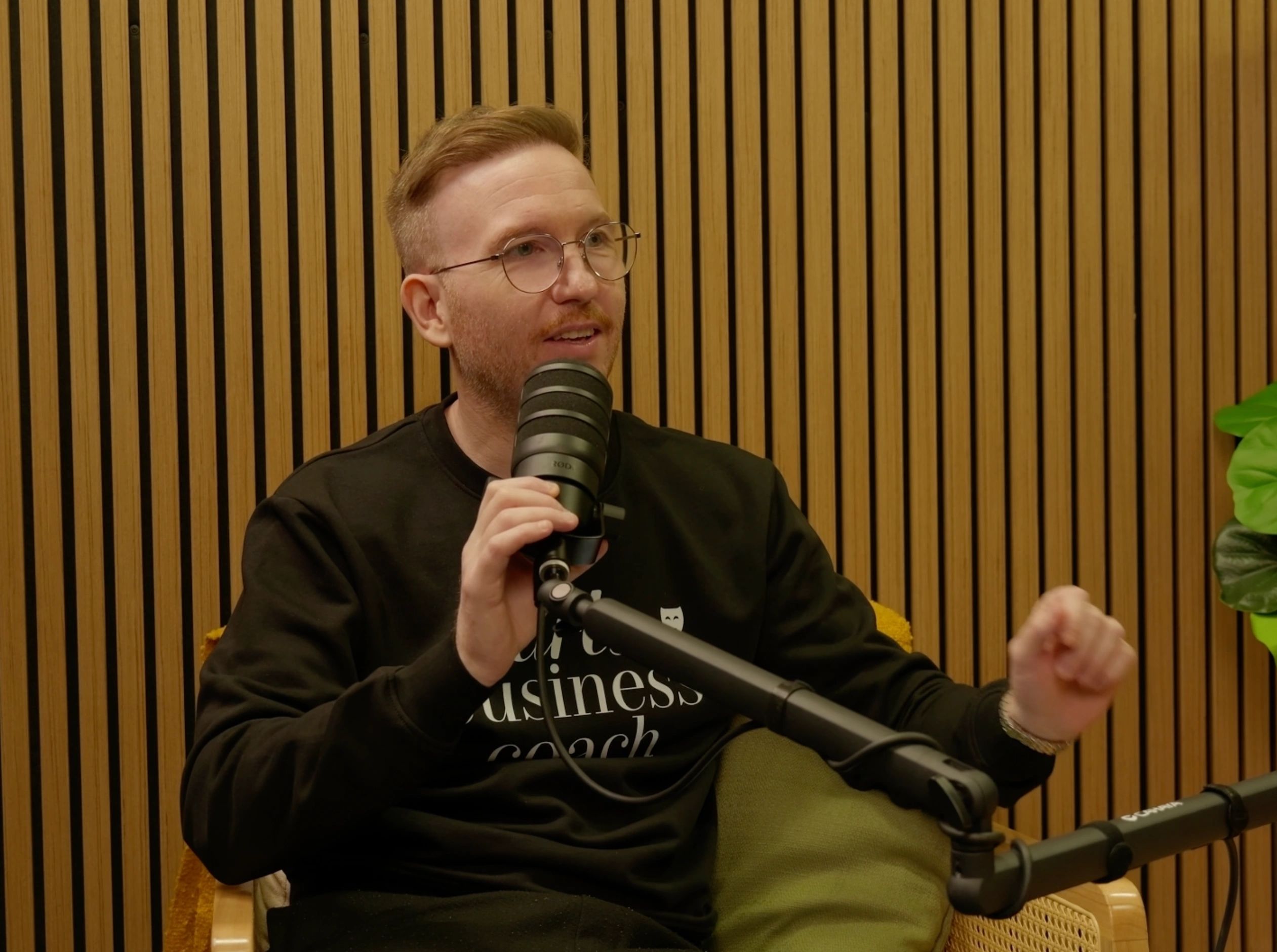 Man speaking into a microphone in a studio with wooden paneling.