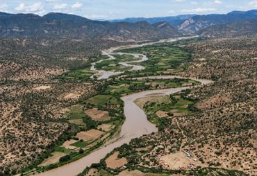 A winding river flows through a green valley surrounded by dry, mountainous terrain.