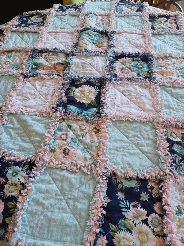 Floral rag quilt with pastel and navy blue squares, edged with pink ruffles.