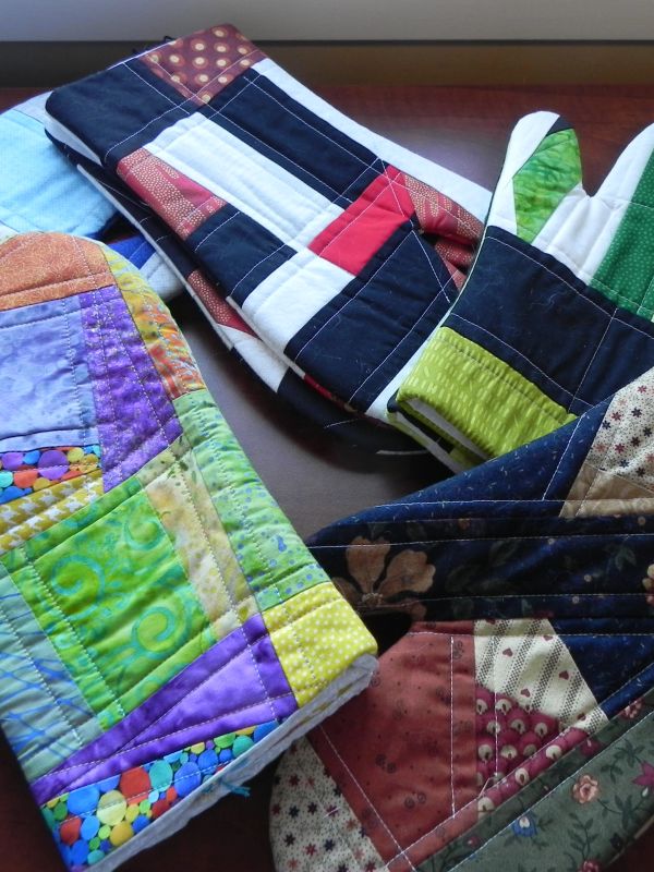 Colorful quilted oven mitts and pot holders with various patchwork designs.