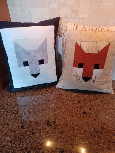 Two decorative pillows with fox face designs in gray and orange colors.