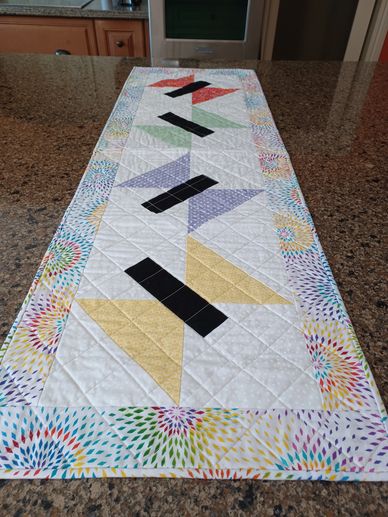 Colorful quilted table runner with geometric patterns on granite countertop.