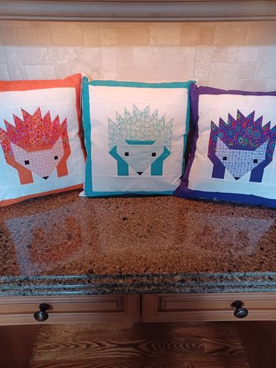 Three colorful hedgehog-patterned cushions arranged on a kitchen counter.