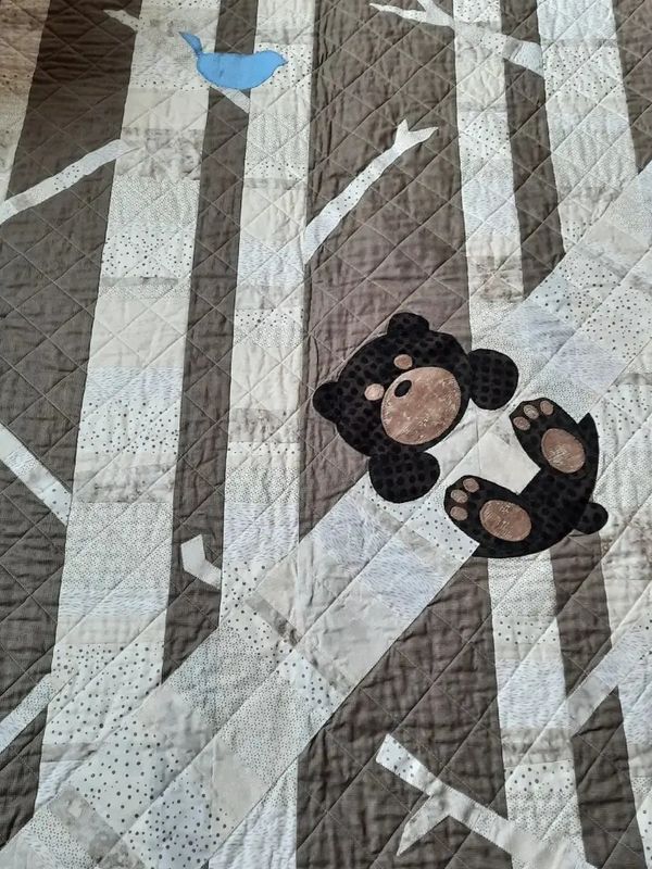 Quilt with a bear and blue bird design on tree trunks.