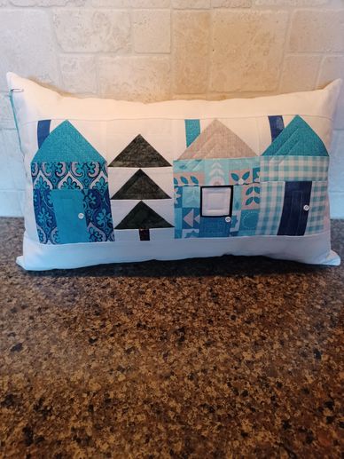 Decorative pillow with patchwork houses and tree design in blue tones.