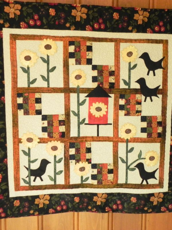 A quilt with sunflowers, birds, and a birdhouse in warm autumn colors.