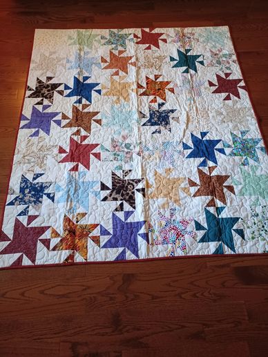 Colorful star-patterned quilt laid on wooden floor.