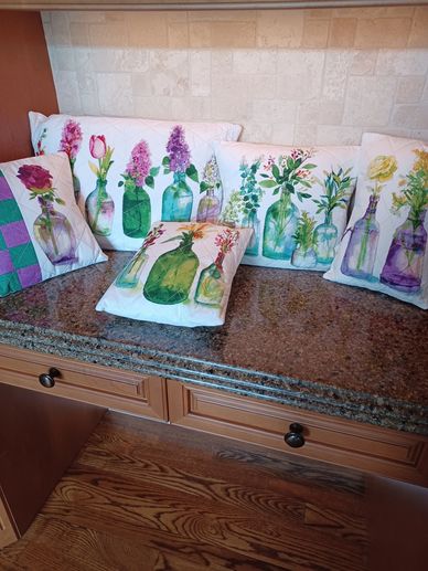 Decorative pillows with watercolor floral bottle designs on a kitchen counter.