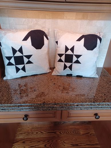 Two white pillows with black geometric star and sheep designs on a kitchen countertop.
