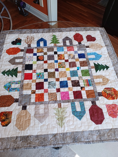 A colorful patchwork quilt with a checkered center and nature-themed appliques around the edges.