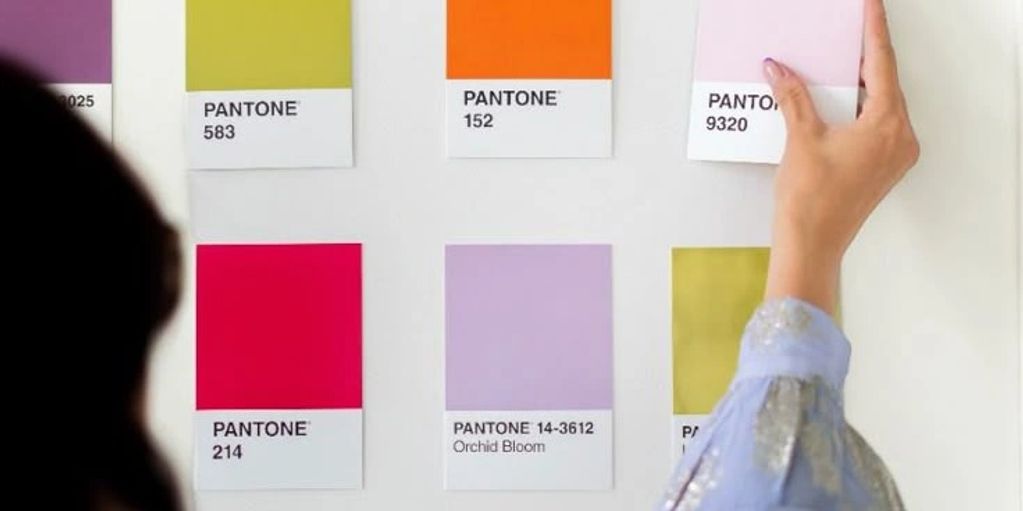 Person arranging Pantone color swatches on a wall.