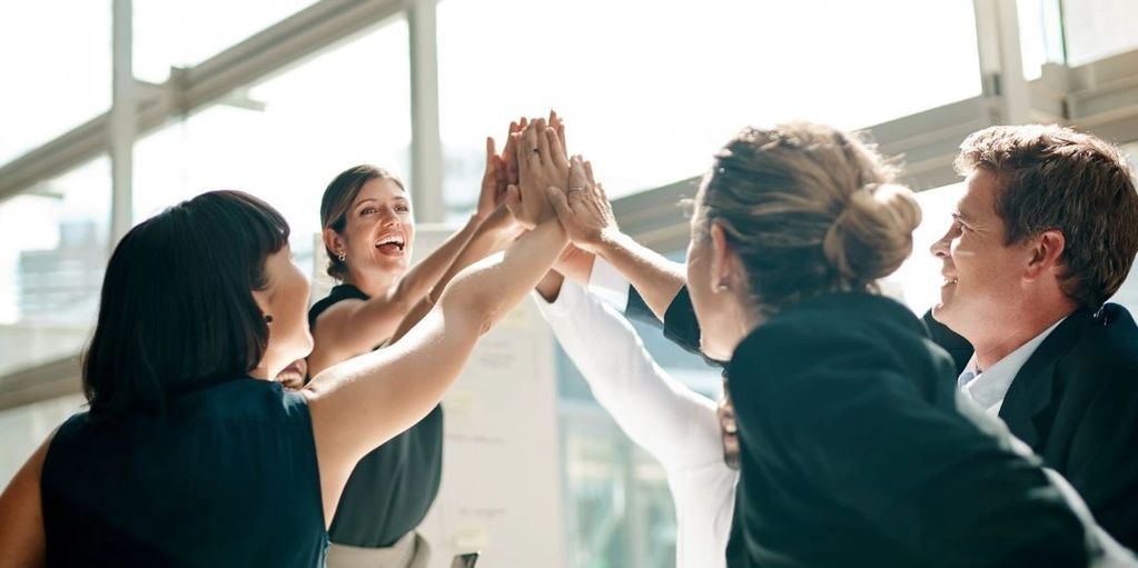A group of colleagues enthusiastically high-fiving in a bright office.