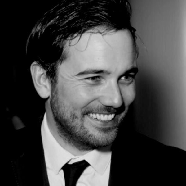 A man in a suit smiling in a black and white photo.