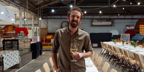 Man smiling and holding a wine glass in a rustic dining hall.