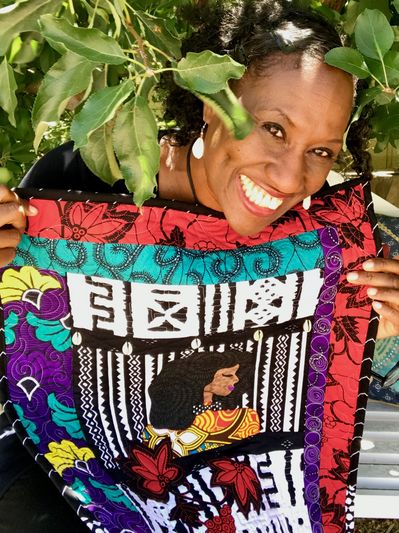 Smiling woman proudly holds colorful African-inspired fabric with intricate designs.