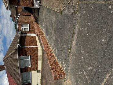 A brick house with a newly built low brick wall along the driveway.