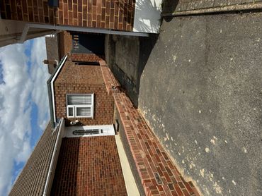 A brick driveway leading to a side entrance of a house under a partly cloudy sky.