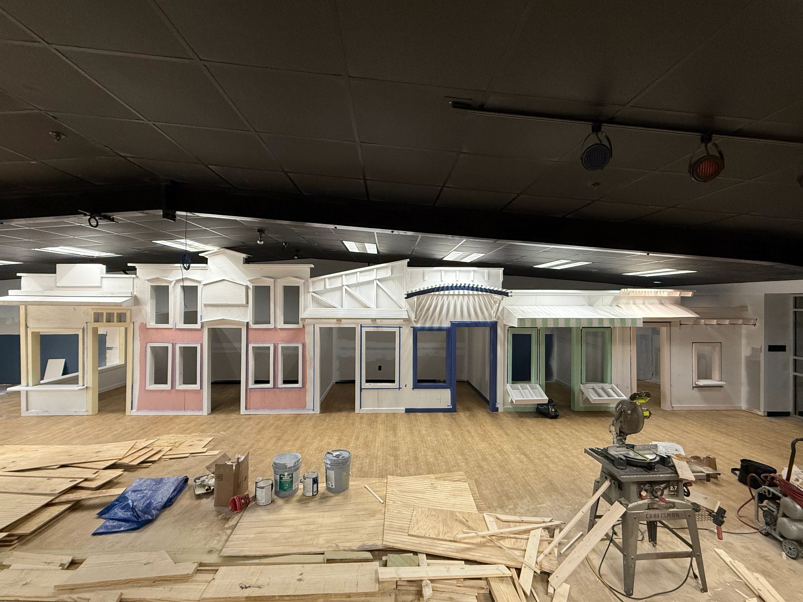 Indoor construction of a row of miniature storefront facades with tools and materials.