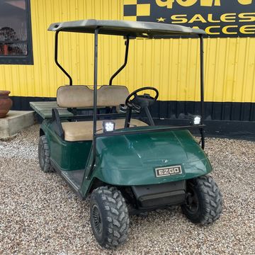 A 1998 Forest Green EZGO TXT with a wooden cargo deck, flood lights, and a gun rack