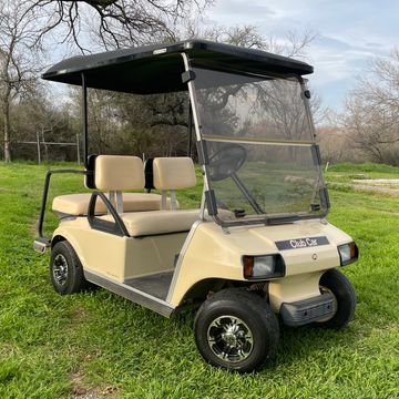 A tan 2003 Club Car DS with a rear flip seat and factory style lights.