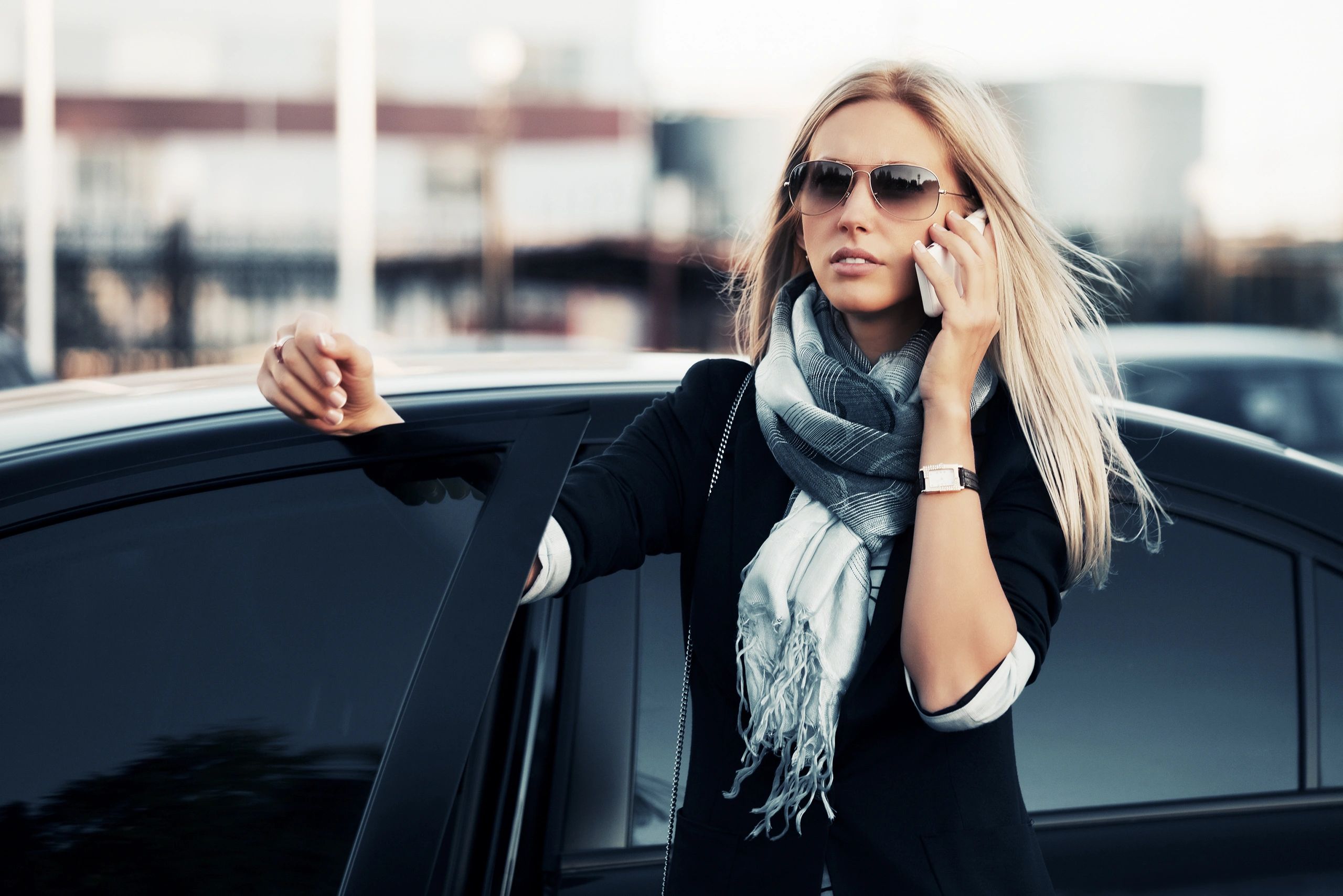 Woman with sunglasses talking on phone by her car door.
