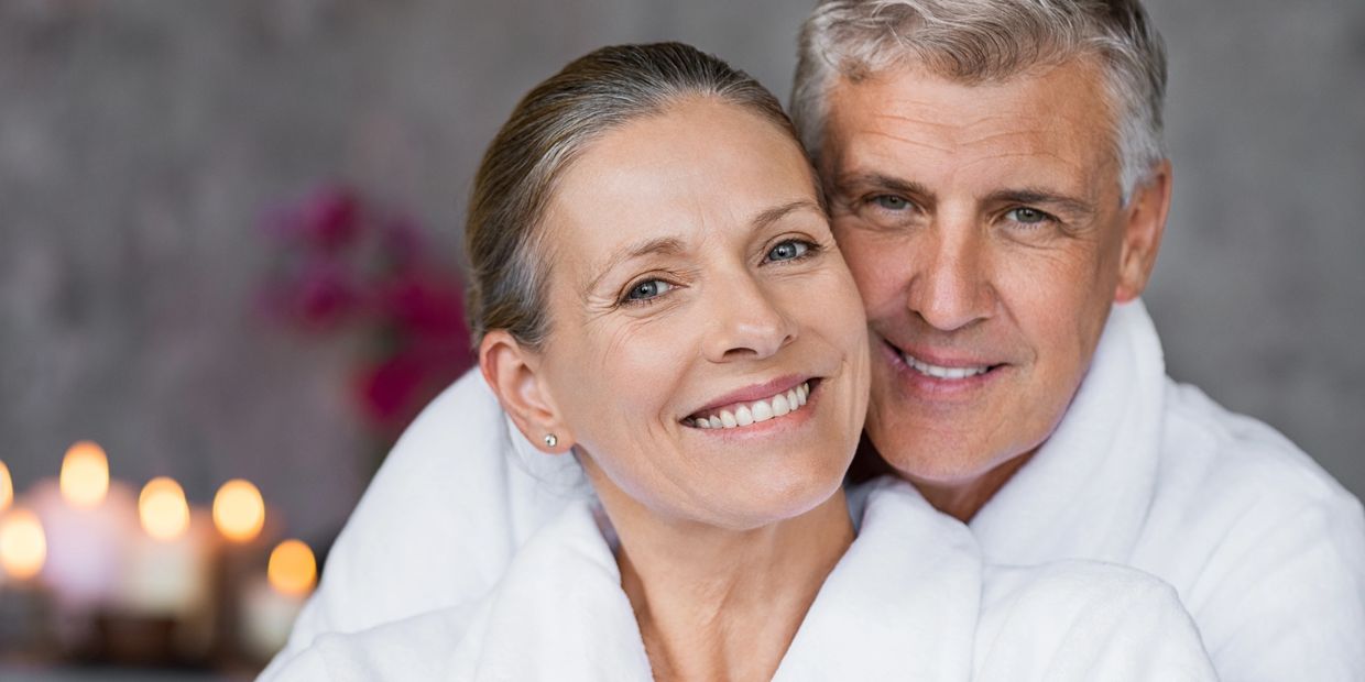 Smiling mature couple in white robes enjoying a relaxing moment together.