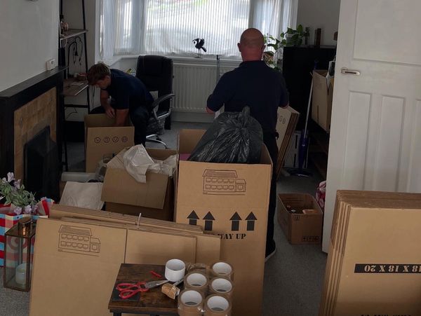 Two people packing boxes in a room filled with packing supplies.