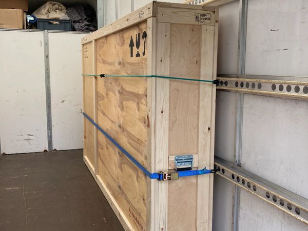 Large wooden crate secured inside a transport vehicle with straps.