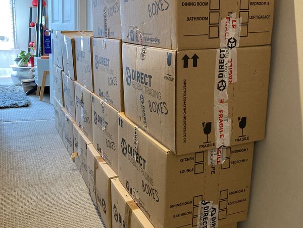 Stacked moving boxes labeled for different rooms in a hallway.